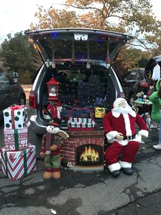 a man dressed as santa claus sitting in the trunk of a car with presents around him