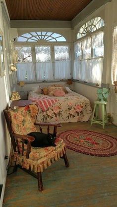 a room with a bed, chair and rugs on the floor in front of two windows