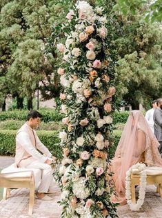 a man and woman sitting on chairs in front of a flower covered arch at a wedding