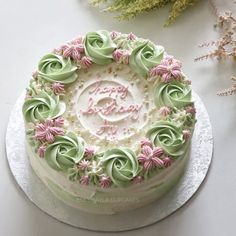 a white cake with green and pink frosting on a silver platter next to flowers