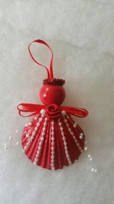 an ornament shaped like a shell with pearls on the bottom and red ribbon hanging from it