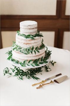 a three tiered cake with greenery on top and two forks next to it