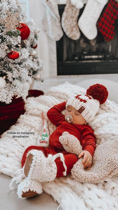 a baby doll is laying on a blanket in front of a christmas tree and stockings