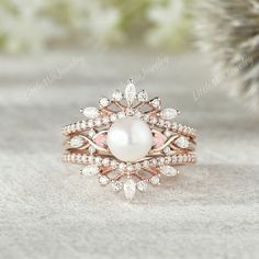 a white pearl and diamond ring set on top of a table with pine cones in the background