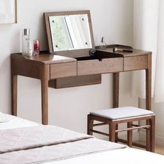 a wooden desk with a mirror and stool in front of a window next to a bed