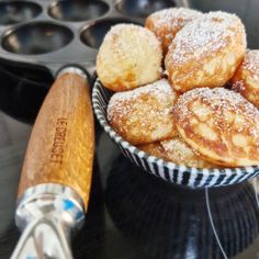 powdered sugar covered donuts in a bowl next to a muffin maker and spatula