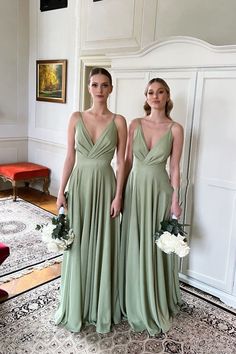 two bridesmaids in sage green dresses standing next to each other and holding bouquets