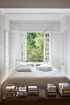 a bed with lots of books on top of it in a bedroom next to a window