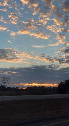 the sun is setting behind some clouds in the sky over an empty road and trees