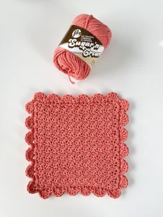 a crochet dishcloth next to a ball of yarn on a white surface