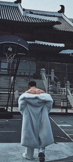 a man in a white fur coat is standing on a basketball court with his back turned to the camera