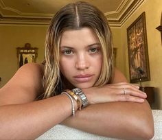 a beautiful young woman sitting on top of a white couch next to a wall with paintings