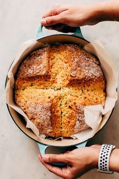 a person holding a loaf of bread in a pan on top of a white table