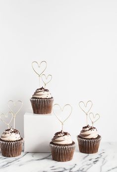 four cupcakes with chocolate frosting and hearts on top are sitting in front of a white box