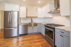 an empty kitchen with stainless steel appliances and white cabinets, wood floors, and hard wood flooring