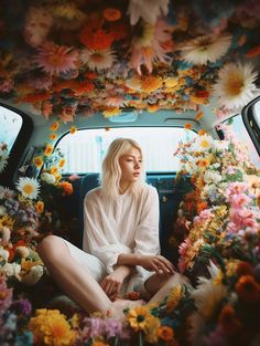 a woman sitting in the back of a car surrounded by flowers