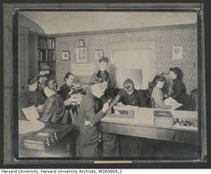 an old black and white photo of people in a room with many books on the table