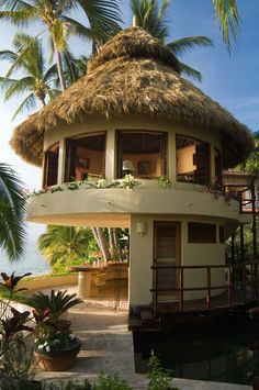 a round house with a thatched roof next to palm trees and the ocean in the background