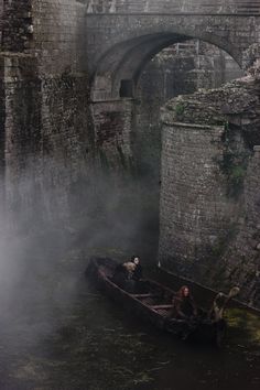 a small boat floating on top of a river next to a stone bridge in the fog