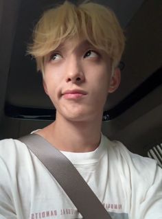 a young man with blonde hair wearing a white shirt and holding a gray seat belt