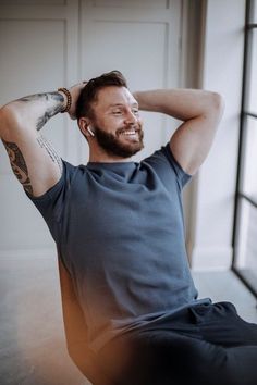 a man sitting on the floor with his hands behind his head and tattoos on his arm