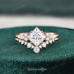 an engagement ring with a princess cut diamond surrounded by smaller round diamonds on a green velvet box