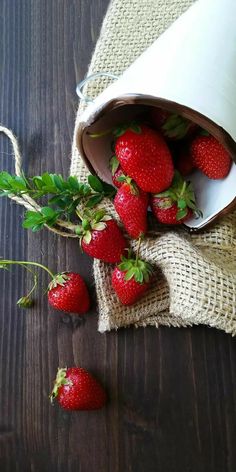 some strawberries are in a white bowl on a wooden table next to a cloth