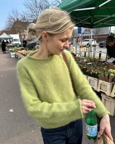 a woman in a green sweater is holding a bottle