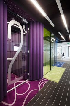 an office with purple and green carpeting, white walls and large window coverings