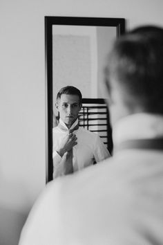 a man is standing in front of a mirror brushing his teeth and adjusting his tie