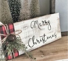 a wooden sign that says merry christmas sitting on top of a table next to evergreen trees