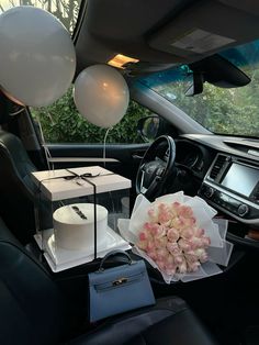 a car with balloons, cake and flowers in the passenger side seat as well as a purse