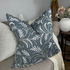 two blue and white pillows sitting on top of a couch next to a vase with flowers