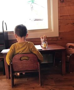 a little boy sitting in a chair looking out the window