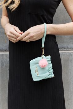 a woman in a black dress holding a blue purse with a pink pom - pom