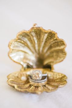 two wedding rings sitting on top of a gold shell shaped ring dish with a diamond center