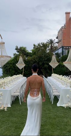 the back of a woman in a wedding dress walking towards tables with umbrellas on them