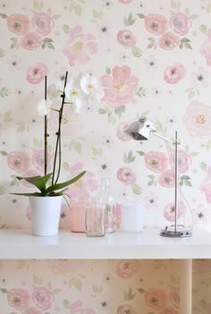 a white table topped with a vase filled with flowers next to a wallpapered wall