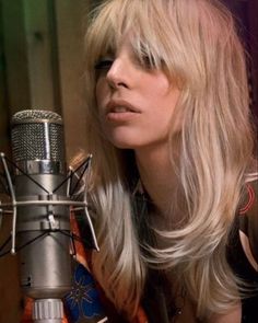 a woman with long blonde hair sitting in front of a microphone and looking off to the side