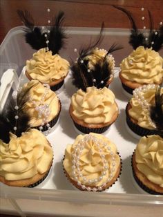 cupcakes with yellow frosting and black feathers in a plastic container on a table