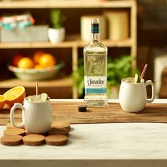 a bottle of gin sits on a table next to two mugs and an orange slice