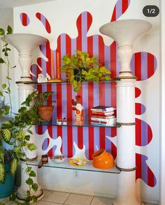 a shelf with plants and books on it in front of a colorful wallpapered background