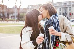 two young women kissing each other while holding coffee cups in their hands on the street