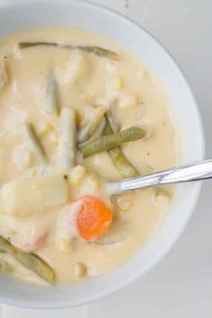 a bowl filled with soup and vegetables on top of a white countertop next to a silver spoon