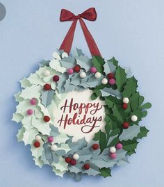 a paper wreath with holly leaves and berries hanging from it's side on a blue background