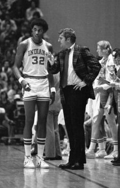 an old black and white photo of two basketball players talking to each other on the court