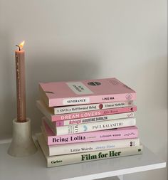 a stack of books sitting on top of a white table next to a lit candle