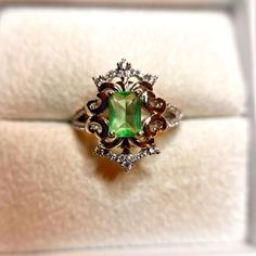 a ring with a green stone surrounded by white diamonds in a gift box on display