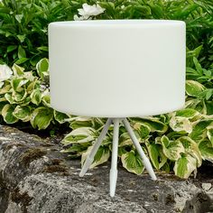 a white table lamp sitting on top of a rock next to plants and flowers in the background