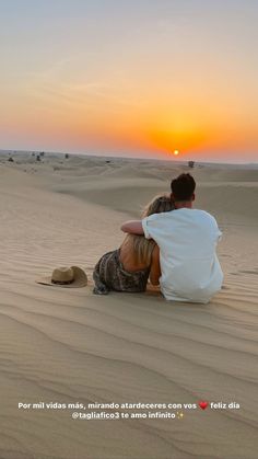 two people sitting on the sand in the desert watching the sun rise over the horizon